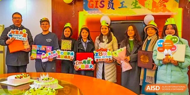 A group of female students or staff posing together in graduation attire and holding colorful signs at a school event at GDUFS International School Guangzhou.