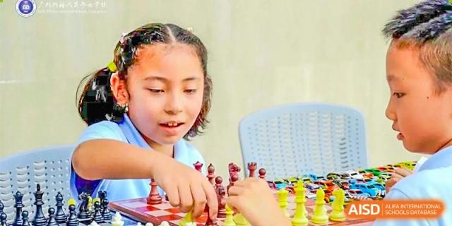 A young female student focused on playing chess in a bright setting at GDUFS International School Guangzhou.