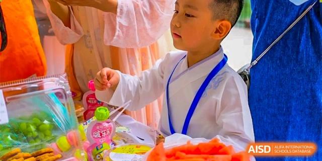 A young male student in traditional-style clothing focusing on an activity or preparing food at GDUFS International School Guangzhou.