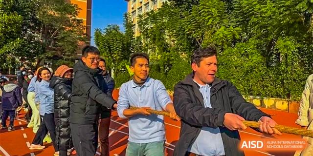 A group of male adults standing together outdoors on a sports field, possibly coaches, staff, or parents at GDUFS International School Guangzhou.
