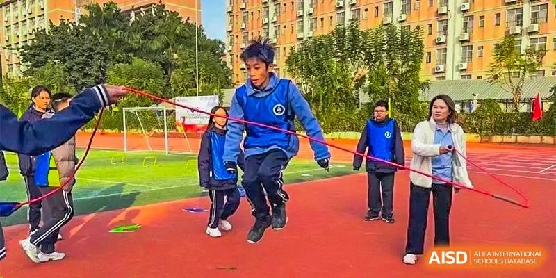 Two young boys skipping rope together on a red outdoor sports surface at GDUFS International School Guangzhou.