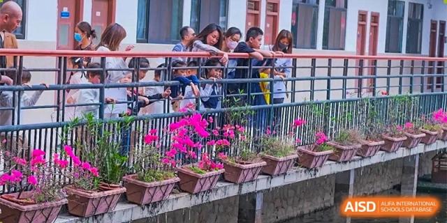 A group of students gathered and looking over a railing with flower boxes in a courtyard or outdoor area at GDUFS International School Guangzhou.