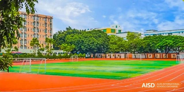 A view of a large green sports field surrounded by a bright orange running track on the campus of GDUFS International School Guangzhou.