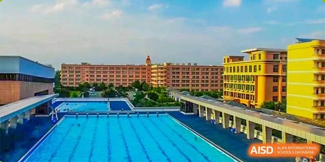 A clear view of a large, outdoor swimming pool next to the red-brick buildings of the campus at GDUFS International School Guangzhou.