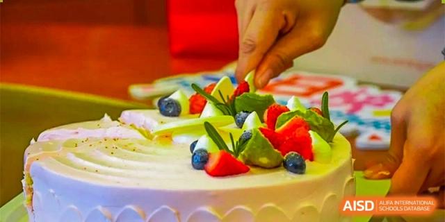GDUFS International School Guangzhou birthday or celebration cake decorated with fresh fruit, including strawberries and blueberries, being cut.