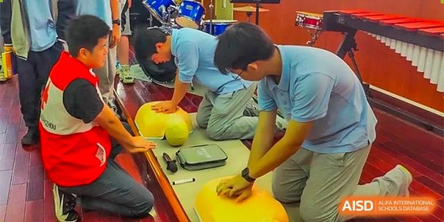 Two GDUFS International School Guangzhou students wearing matching blue shirts kneeling down and working on an activity with large, yellow, spherical objects.