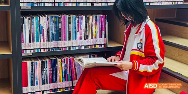 A Guiyang Prime School student browsing or reading a book in front of a full bookshelf in the school library.