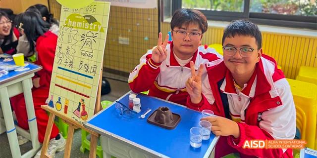A Guiyang Prime School student in a red uniform working on a science experiment or hands-on activity at a small table.