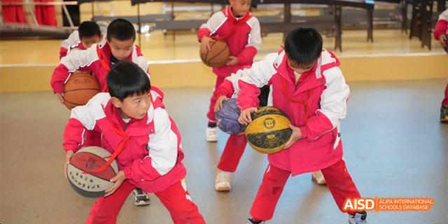 Young students from Guiyang Prime School wearing red and white uniforms, participating in a basketball drill or game indoors.