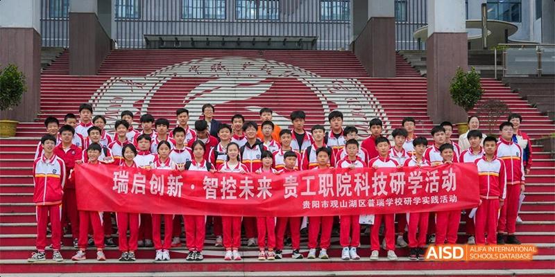 A large group of Guiyang Prime School students and teachers posing for a group photo on the red stadium steps, holding a commemorative banner.