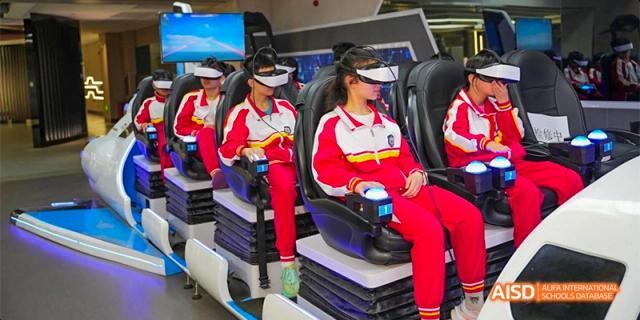 Guiyang Prime School students wearing red and white uniforms and VR headsets, seated in simulation chairs for a technology or educational activity.