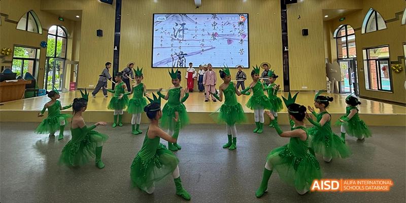 Young students from Guiyang Prime School performing a dance or stage routine in bright green costumes.