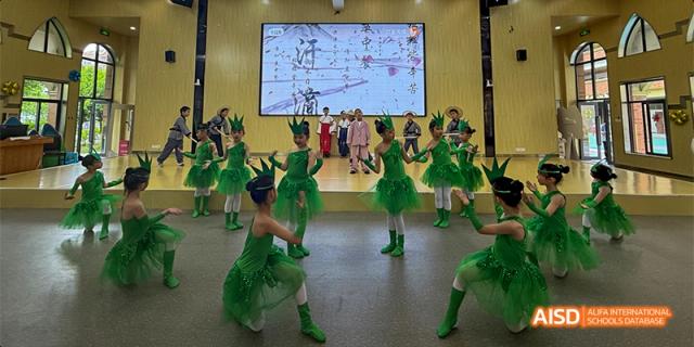 Young students from Guiyang Prime School performing a dance or stage routine in bright green costumes.