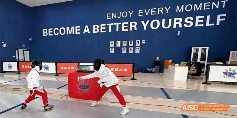 A Guiyang Prime School student striking a pose in front of a blue wall with the motivational phrase "ENJOY EVERY MOMENT. BE A BETTER YOURSELF."