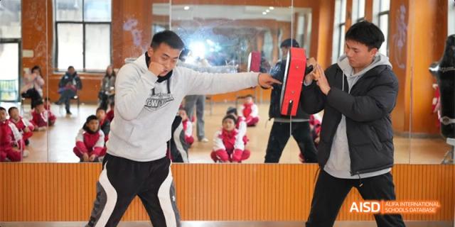 A Guiyang Prime School student practicing martial arts or boxing indoors, hitting a padded target held by an instructor.