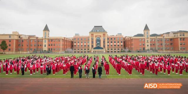 A large group of Guiyang Prime School students dressed in red uniforms standing in a formation on the grounds in front of the main school building.