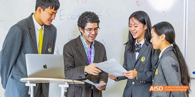 A teacher in a blazer reviews documents with two students in front of a whiteboard labeled Economics at Beijing Haidian Kaiwen Academy.