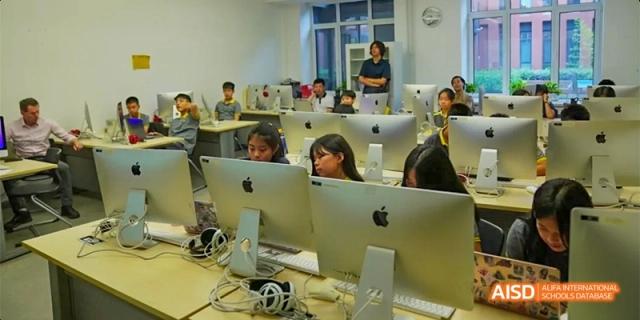 Students work on large desktop computers in a dedicated technology lab with a teacher supervising at Beijing Haidian Kaiwen Academy.