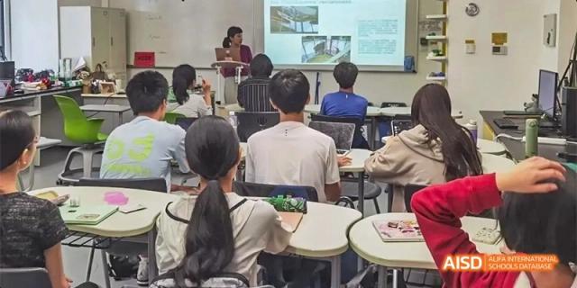 Students sit at curved desks watching a presentation on a large screen at the front of the room at Beijing Haidian Kaiwen Academy.