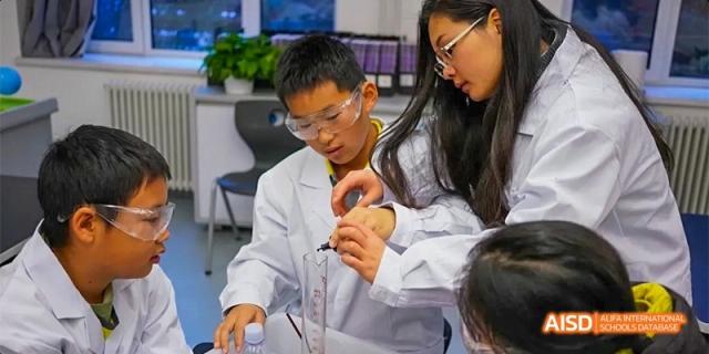 A group of students in protective gear work together to measure liquids in a beaker during chemistry at Beijing Haidian Kaiwen Academy.