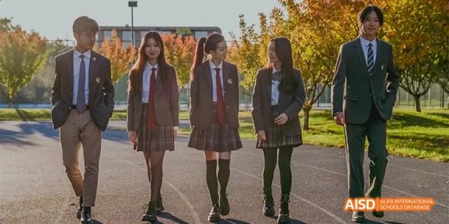 Three students in school uniforms walk together outside on a path surrounded by autumn trees at Beijing Haidian Kaiwen Academy.