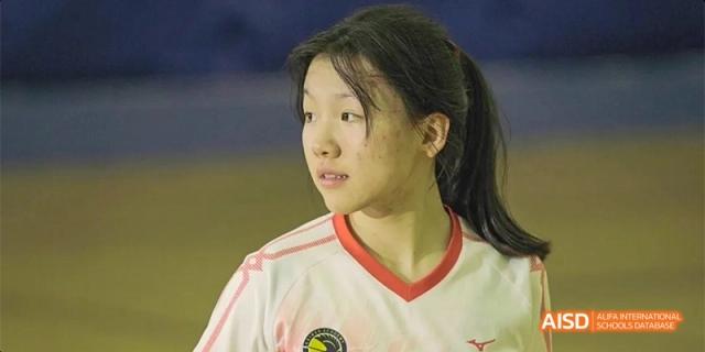 A close-up portrait of a female student wearing a white and red athletic jersey, looking thoughtfully off-camera during a sports event at Beijing Haidian Kaiwen Academy.
