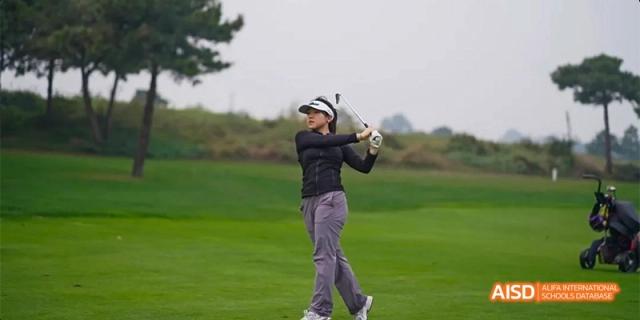 A female student in athletic wear demonstrates a focused golf swing on a wide, well-maintained green fairway under a soft sky at Beijing Haidian Kaiwen Academy.