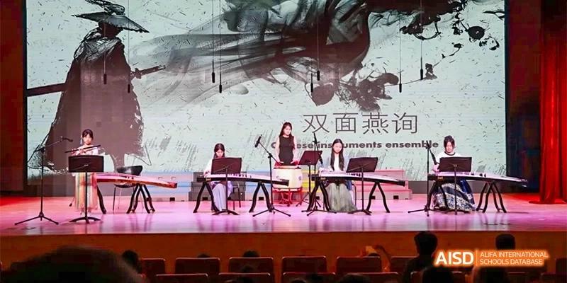 Students perform a traditional musical piece using instruments like the guzheng on a professional stage with artistic backdrops at Beijing Haidian Kaiwen Academy.