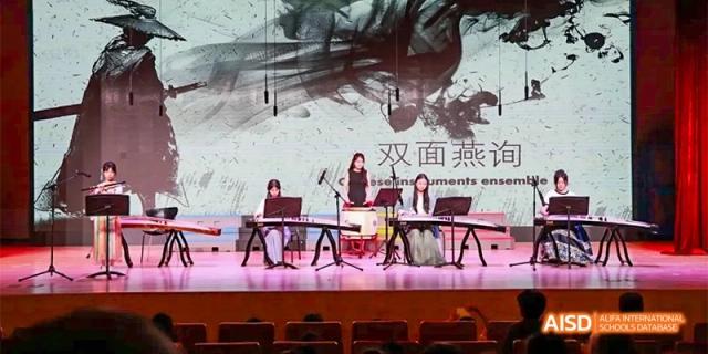 Students perform a traditional musical piece using instruments like the guzheng on a professional stage with artistic backdrops at Beijing Haidian Kaiwen Academy.