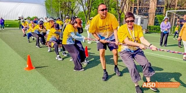 A team of staff and students in yellow shirts work together during a high-energy tug-of-war competition on an outdoor field at Beijing Haidian Kaiwen Academy.