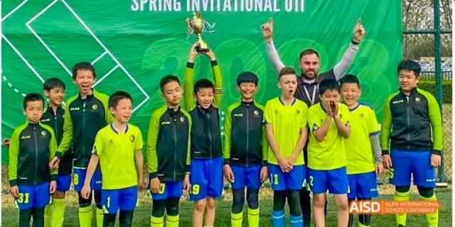 A group of young male athletes in vibrant yellow and green soccer jerseys standing in a line for a team photo on a sports field at Beijing Haidian Kaiwen Academy.