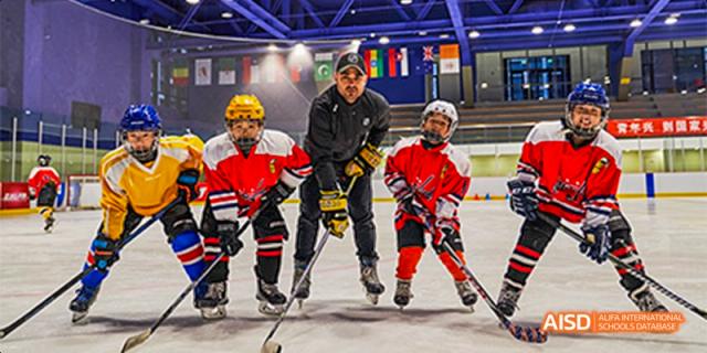 Youth ice hockey players in full red and yellow gear standing on the ice with their coach, holding sticks and ready for a practice session at Beijing Haidian Kaiwen Academy.