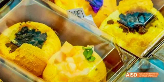 Yellow steamed cakes topped with fresh garnishes and fruit pieces are displayed in clear plastic packaging at Beijing Haidian Kaiwen Academy.