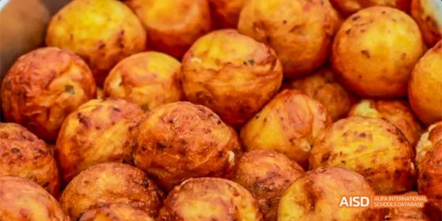 A close-up view of golden-brown, crispy takoyaki or fried dough balls piled together as a snack option at Beijing Haidian Kaiwen Academy.