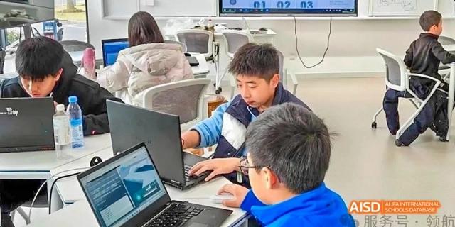 Two male students at Hangzhou World Foreign Language School are working together on a laptop in a classroom.