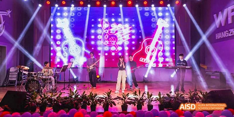 Students at Hangzhou World Foreign Language School are performing a rock concert on a stage, with bright lights and musical instruments.