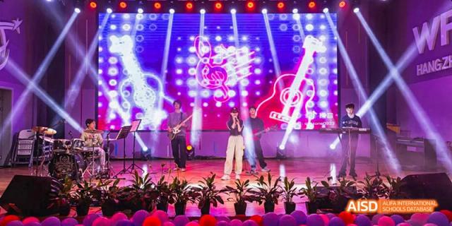 Students at Hangzhou World Foreign Language School are performing a rock concert on a stage, with bright lights and musical instruments.