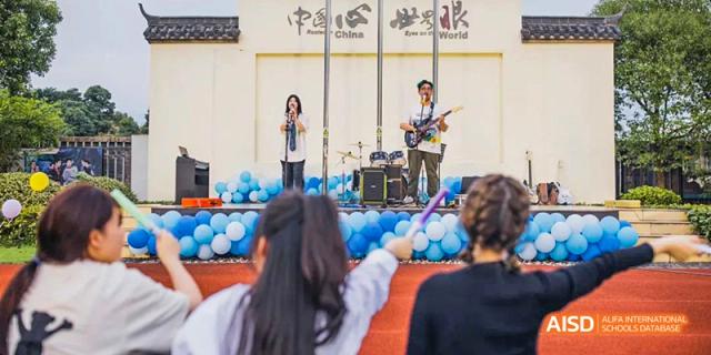 A band is performing on a stage outdoors for a crowd of students at Hangzhou World Foreign Language School.