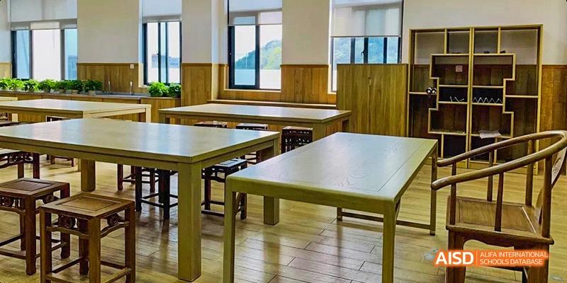 An empty classroom with wooden desks and chairs, a large window, and scenic views at Hangzhou World Foreign Language School.