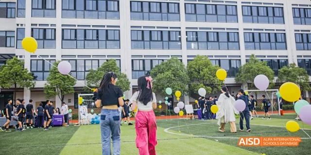 Students at Hangzhou World Foreign Language School are gathered on a lawn outside of a school building, with balloons and decorations.