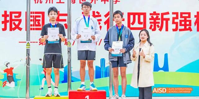 Two male students at Hangzhou World Foreign Language School are standing on a podium and holding medals.