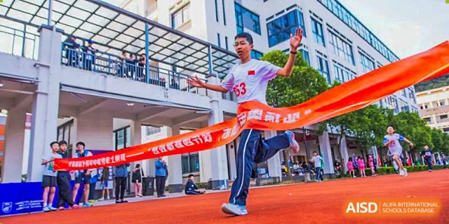 A student at Hangzhou World Foreign Language School is crossing the finish line in a race, with a banner in the background.
