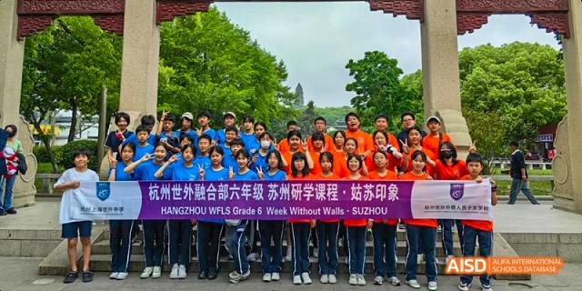 A group of students and teachers from Hangzhou World Foreign Language School are posing for a group photo outdoors with a banner.