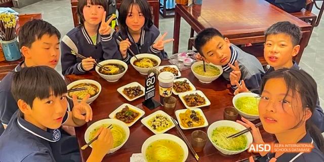 Two students at Hangzhou World Foreign Language School are holding dishes filled with food.