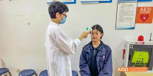 A student at Hangzhou World Foreign Language School is being checked for a temperature with a forehead thermometer.