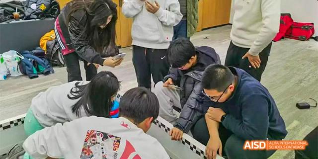 Students huddle together outdoors, focusing on a robotic device or competition track during a hands-on STEM activity at Hefei No.8 High School.