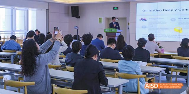 An audience of students and faculty watch a formal presentation given by a speaker at a wooden podium in a large lecture hall at Hefei No.8 High School.