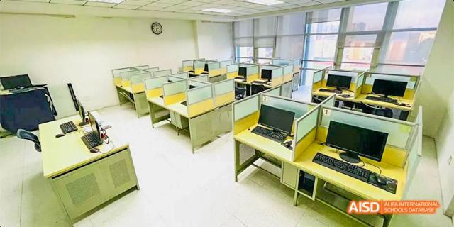 A modern computer lab with rows of yellow cubicle desks and desktop monitors sits ready for students. Hefei No.8 High School.