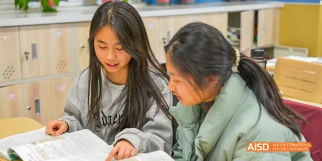 Two students lean in close together to review a textbook during a shared study session in a bright classroom. Hefei No.8 High School.