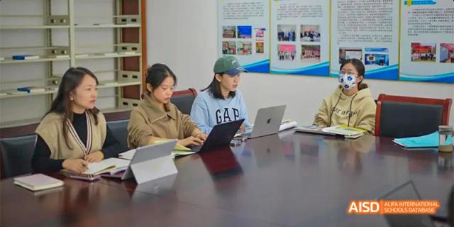 Three students work on laptops and tablets while seated at a large conference table during a group meeting. Hefei No.8 High School.